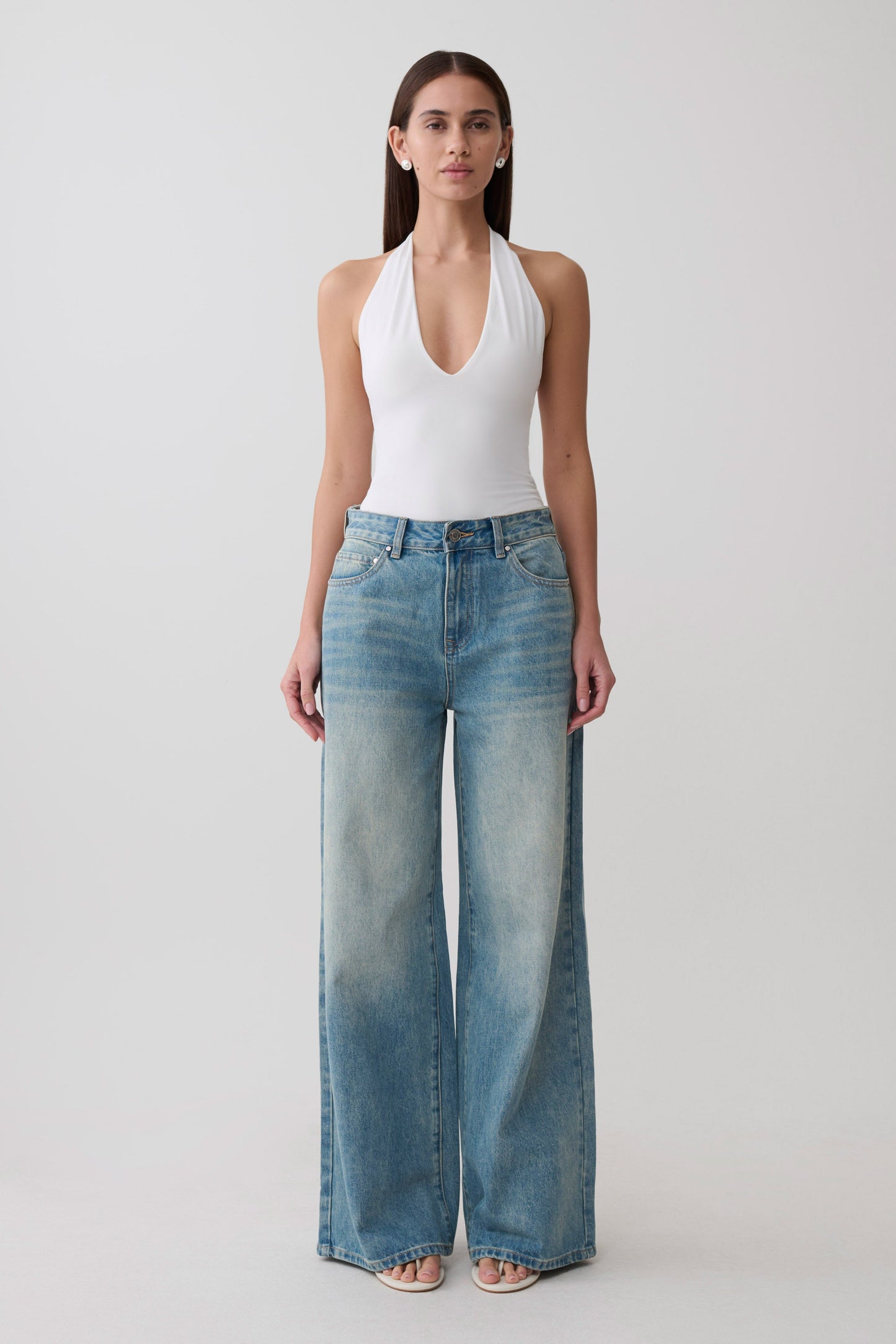 Woman wearing a white slinky halter bodysuit paired with jeans.