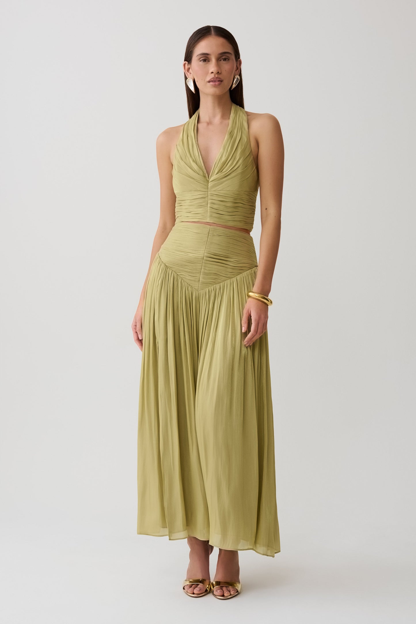 Woman wearing a green gathered v neck top with matching gathered midi skirt.
