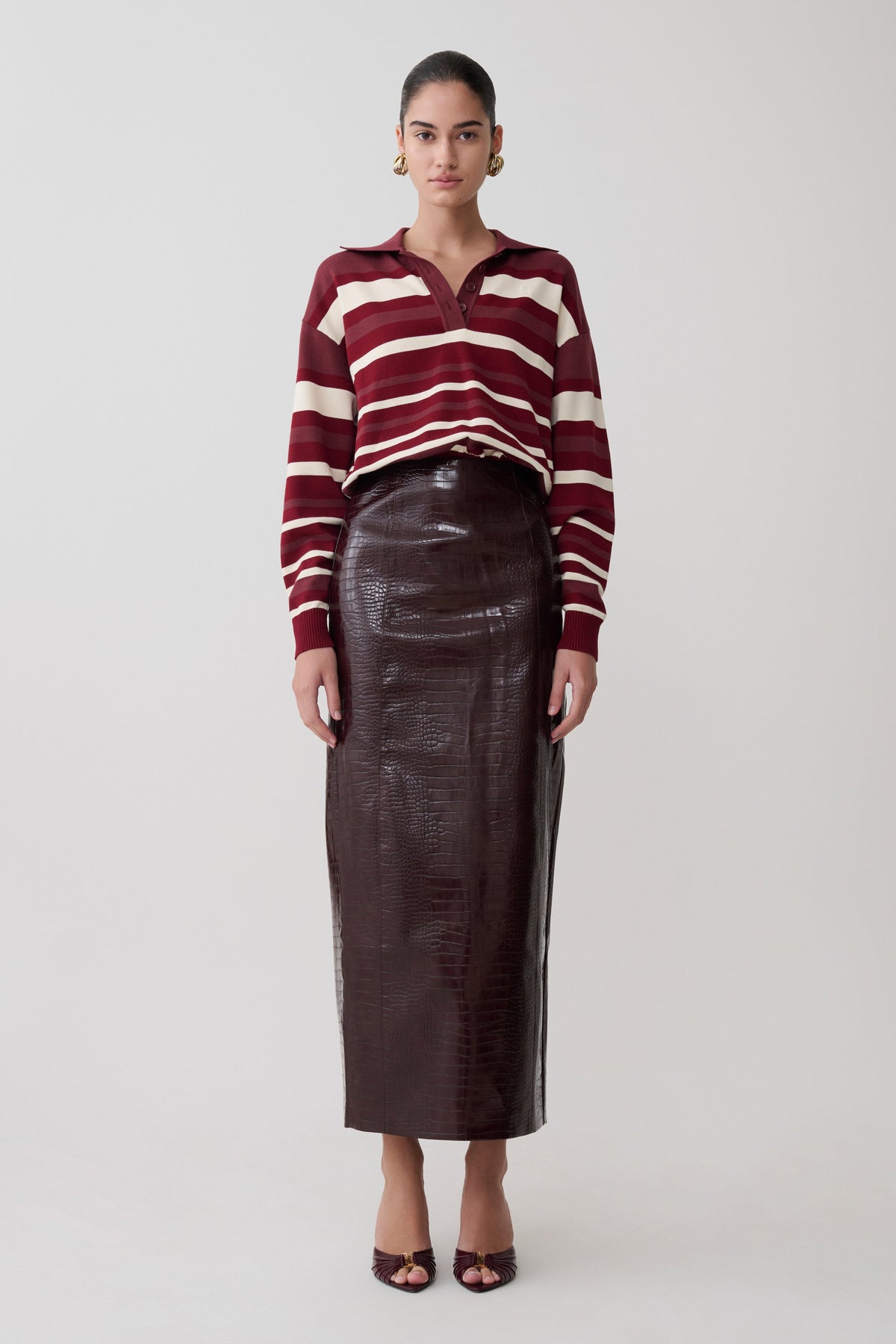 Woman wearing a striped sweater and leather skirt on a white background.