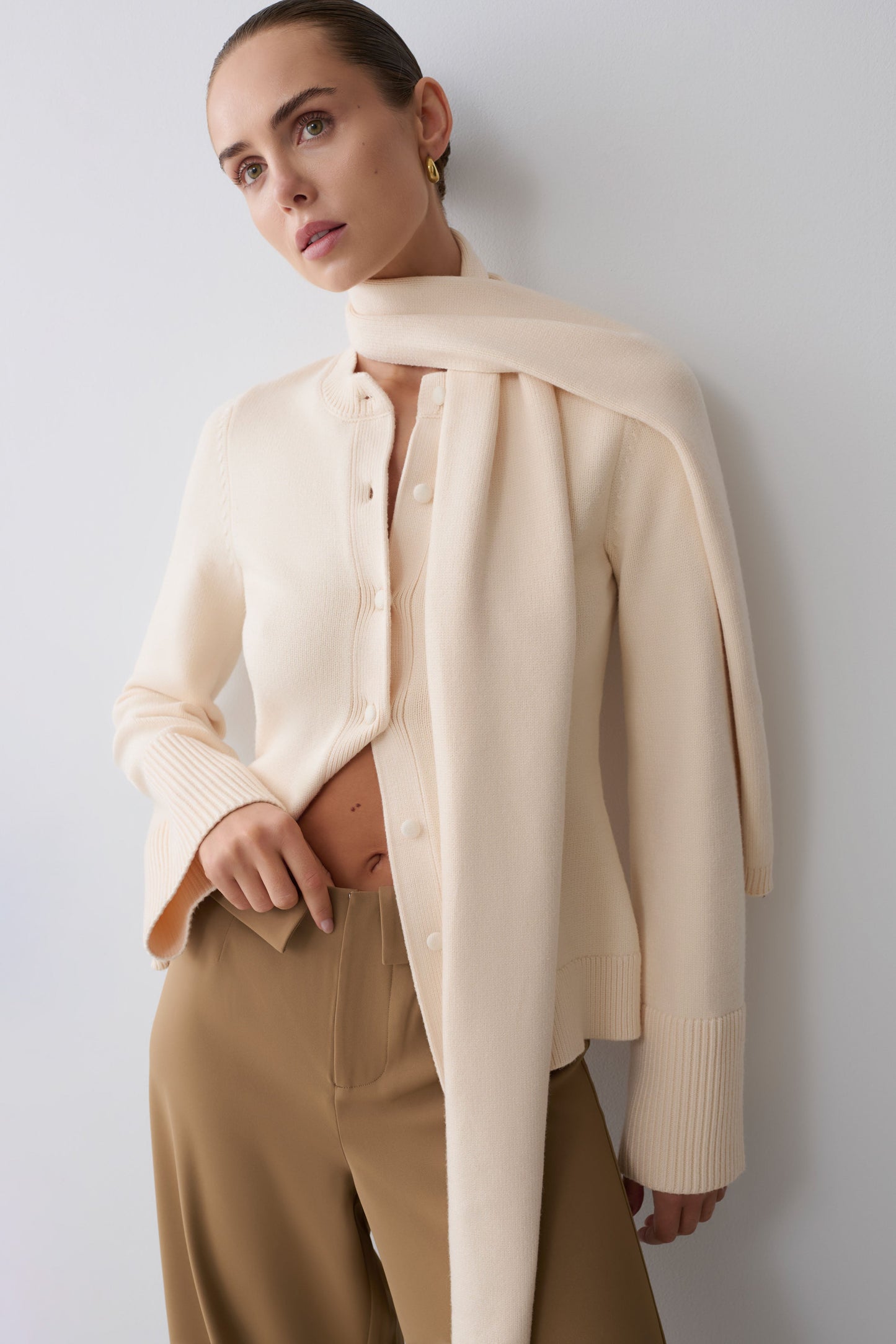 Woman wearing a beige cardigan with scarf.