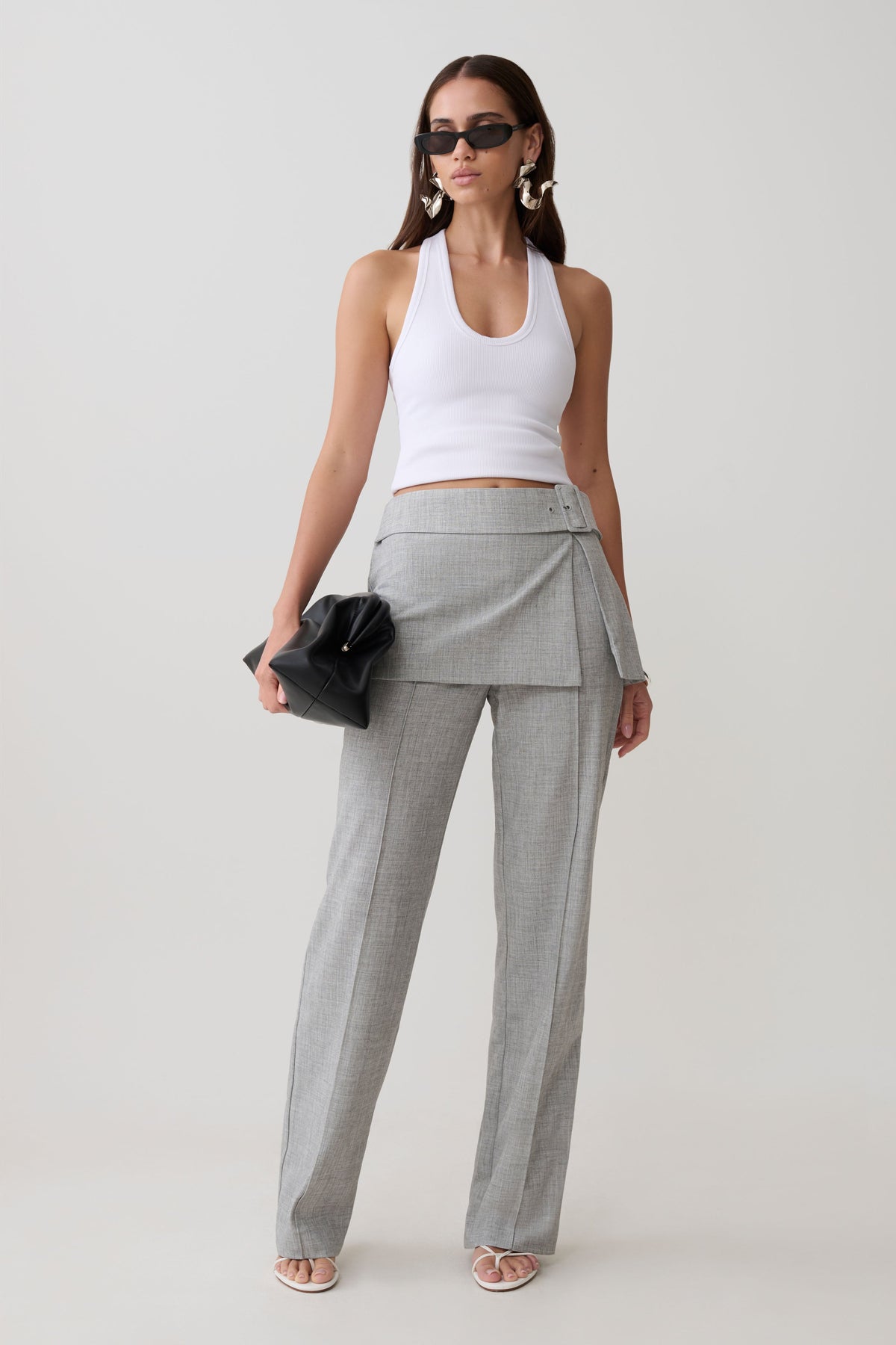 Woman wearing a white tank top and gray wrap skirt straight leg pants.