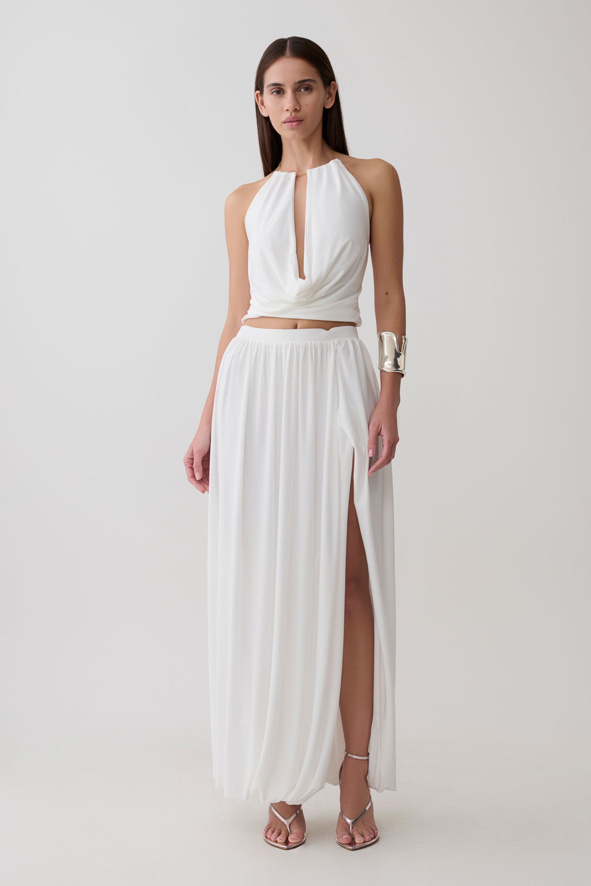 Woman wearing a white halter neck top with hardware and a matching bubble hem midi skirt.