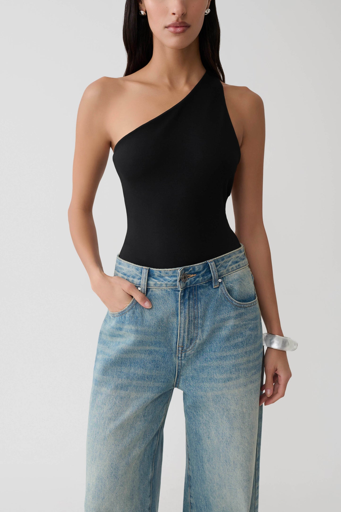 Woman wearing a black asymmetric back ponte bodysuit.