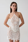 Woman wearing white crochet halter top with matching mini skirt.
