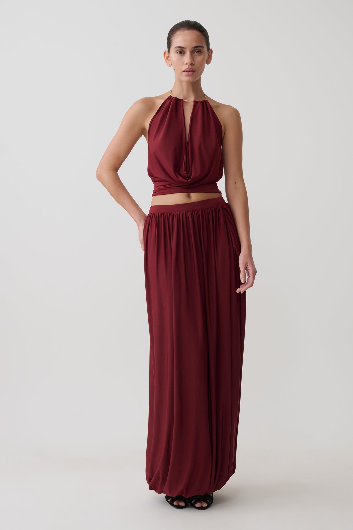 Woman wearing a dark red halter neck top with matching bubble hem midi skirt.