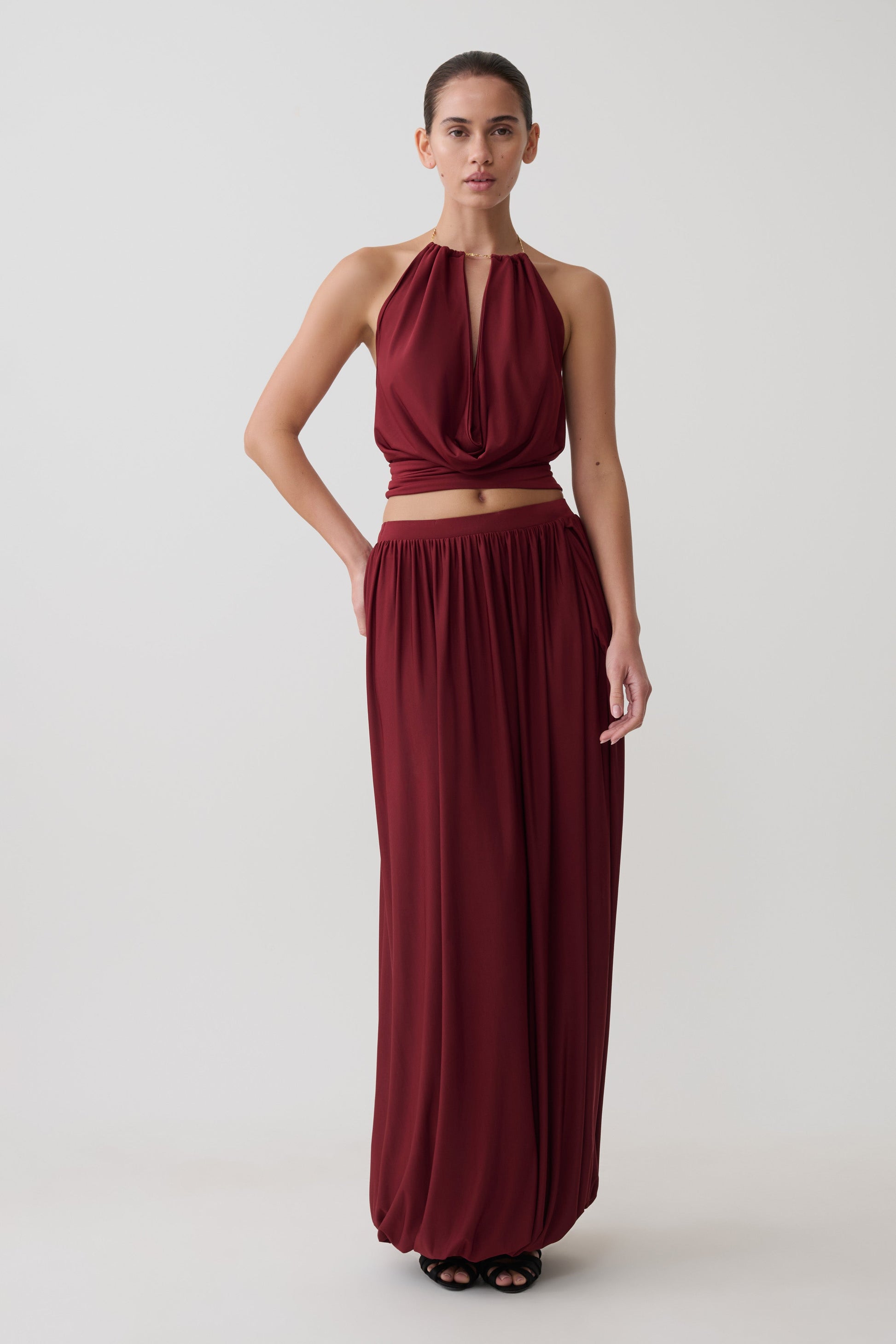 Woman wearing a dark red halter neck top with matching bubble hem midi skirt.