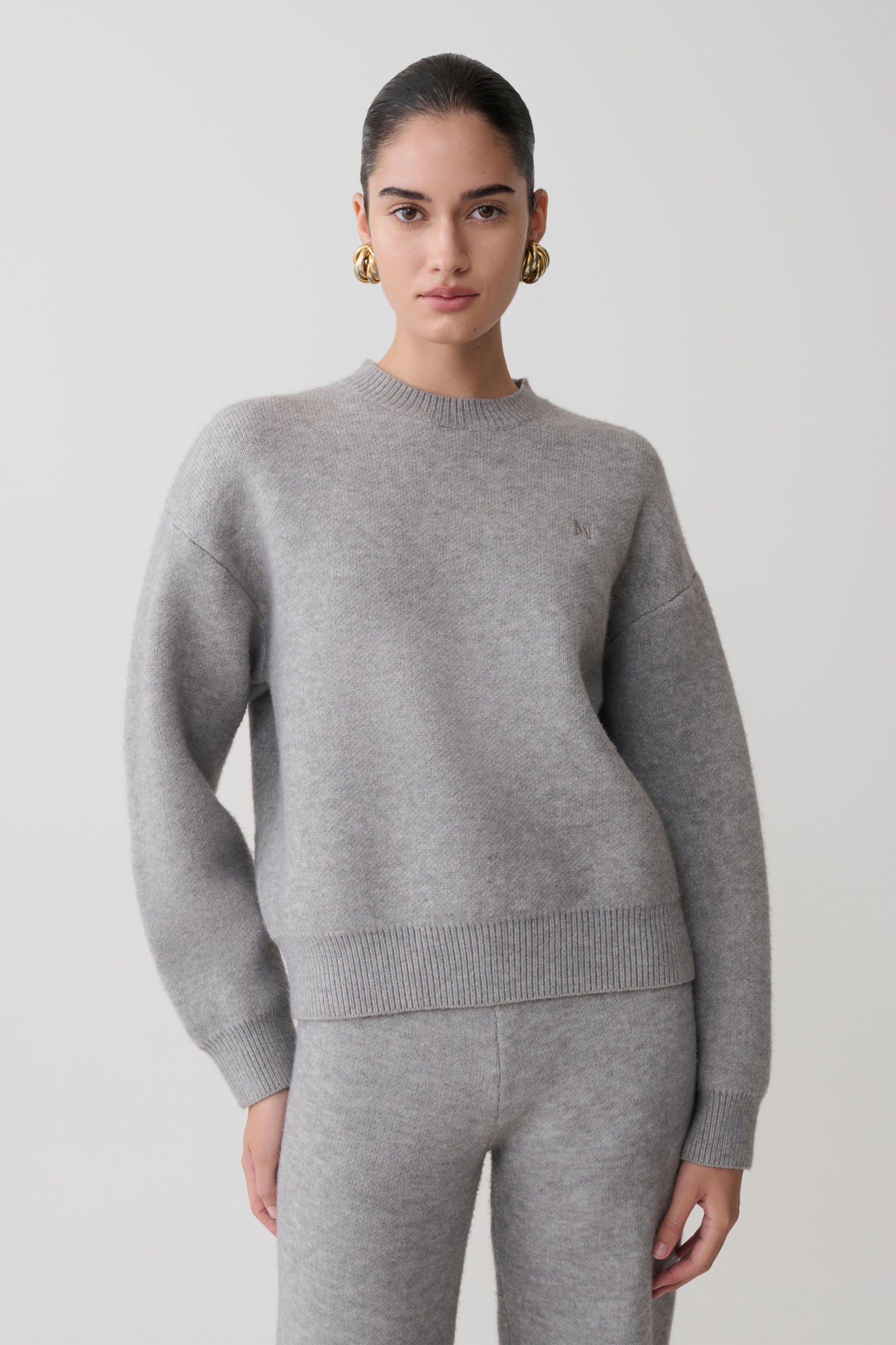 Woman wearing a gray sweater and pants on a plain background.