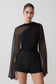 Woman wearing a black outfit with sheer sleeves on a plain background.