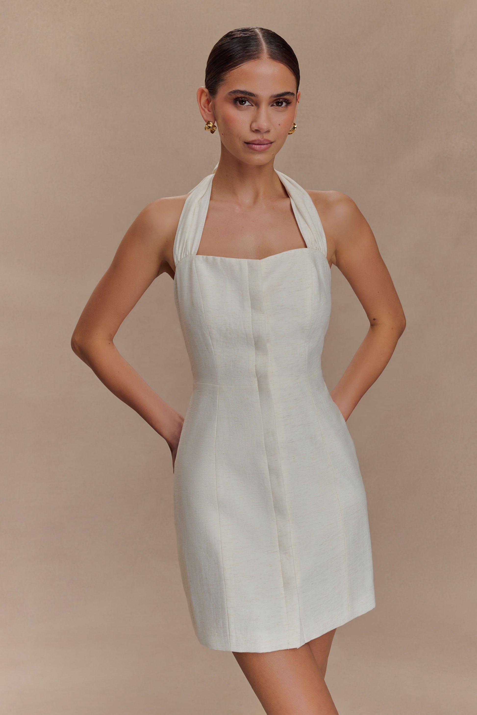 Woman wearing a white halter neck dress against a beige background