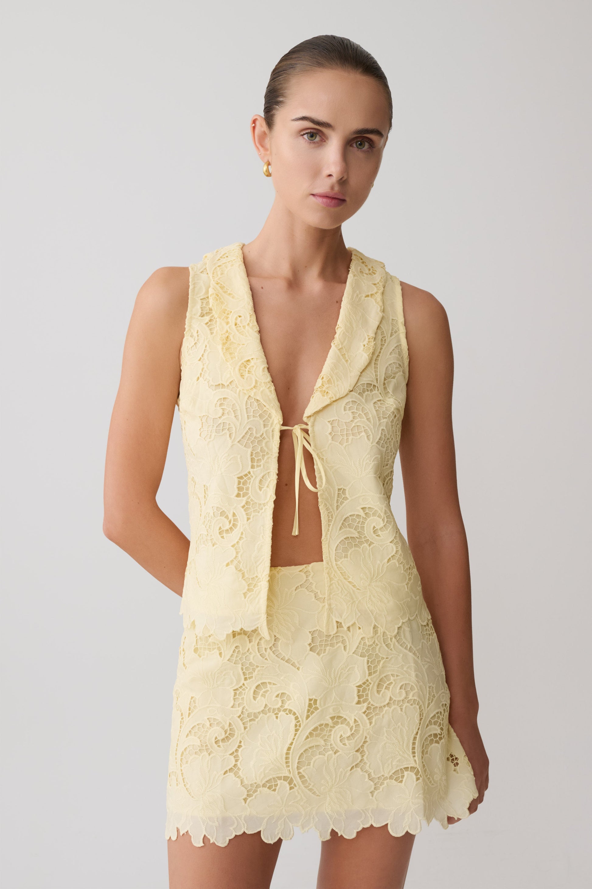 Woman wearing a yellow broderie tie top with matching mini skirt.