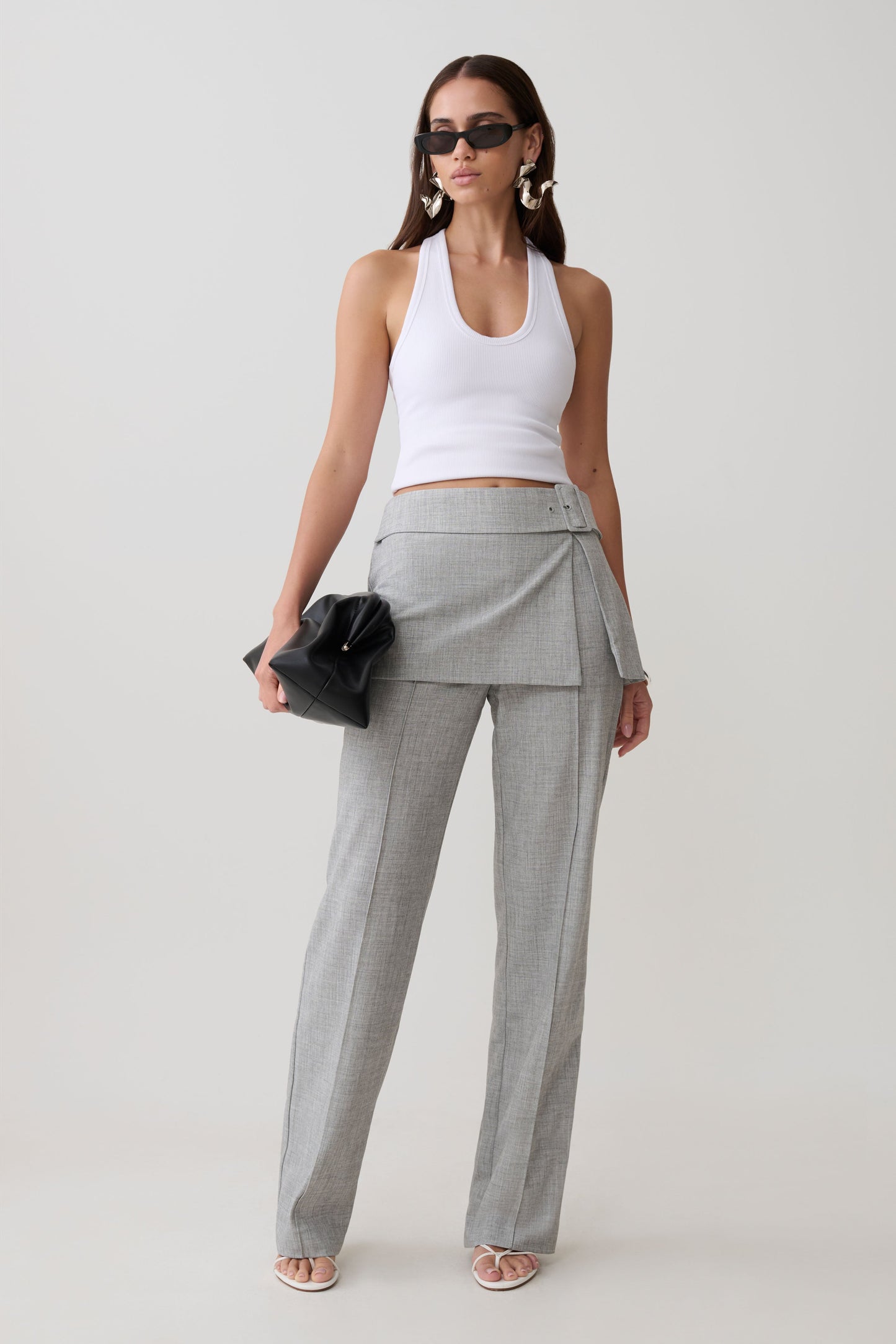 Woman wearing a white tank top and gray  wrap skirt straight leg pants.