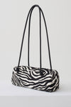 A zebra-print cylindrical shoulder bag with black double shoulder straps, displayed on a clean white studio background.