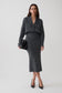 A woman modeling a dark gray knit long-sleeve dress, styled with black pointed-toe heels and a black clutch bag against a light gray studio background.