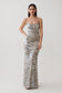 A woman modeling a floor-length, spaghetti-strap sequin gown with a beige, silver, and black animal-stripe pattern against a plain light gray studio background.