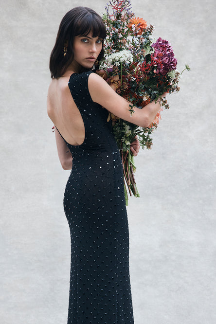 Woman in a black dress holding a bouquet of flowers against a light gray background.