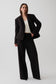 A model wearing a black tailored blazer and matching wide-leg trousers over a cream ribbed top, standing against a light gray studio background.