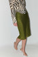 A model wearing a shimmering olive green sequined midi skirt paired with a black and white zebra print long-sleeve top and clear high-heeled sandals, shown against a plain light gray studio background.