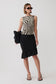 A woman modeling a sleeveless top with a beige and black zebra pattern and a black ruffled midi skirt, paired with black sandals, against a plain light gray studio background.
