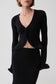 A model wearing a black long-sleeve knit cardigan with a deep V-neck and flared cuffs, paired with a matching black skirt, against a light gray studio background.