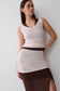 A woman modeling a sleeveless wrap-style top and matching skirt set in cream and dark brown, photographed against a plain light gray studio background.