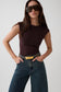 A woman modeling a fitted sleeveless dark brown bodysuit with blue jeans and a gold belt, wearing oversized dark sunglasses against a light gray studio background.