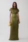 A woman modeling a floor-length olive green satin dress with short cap sleeves and a draped waist detail, holding a small metallic gold clutch against a light gray studio background.